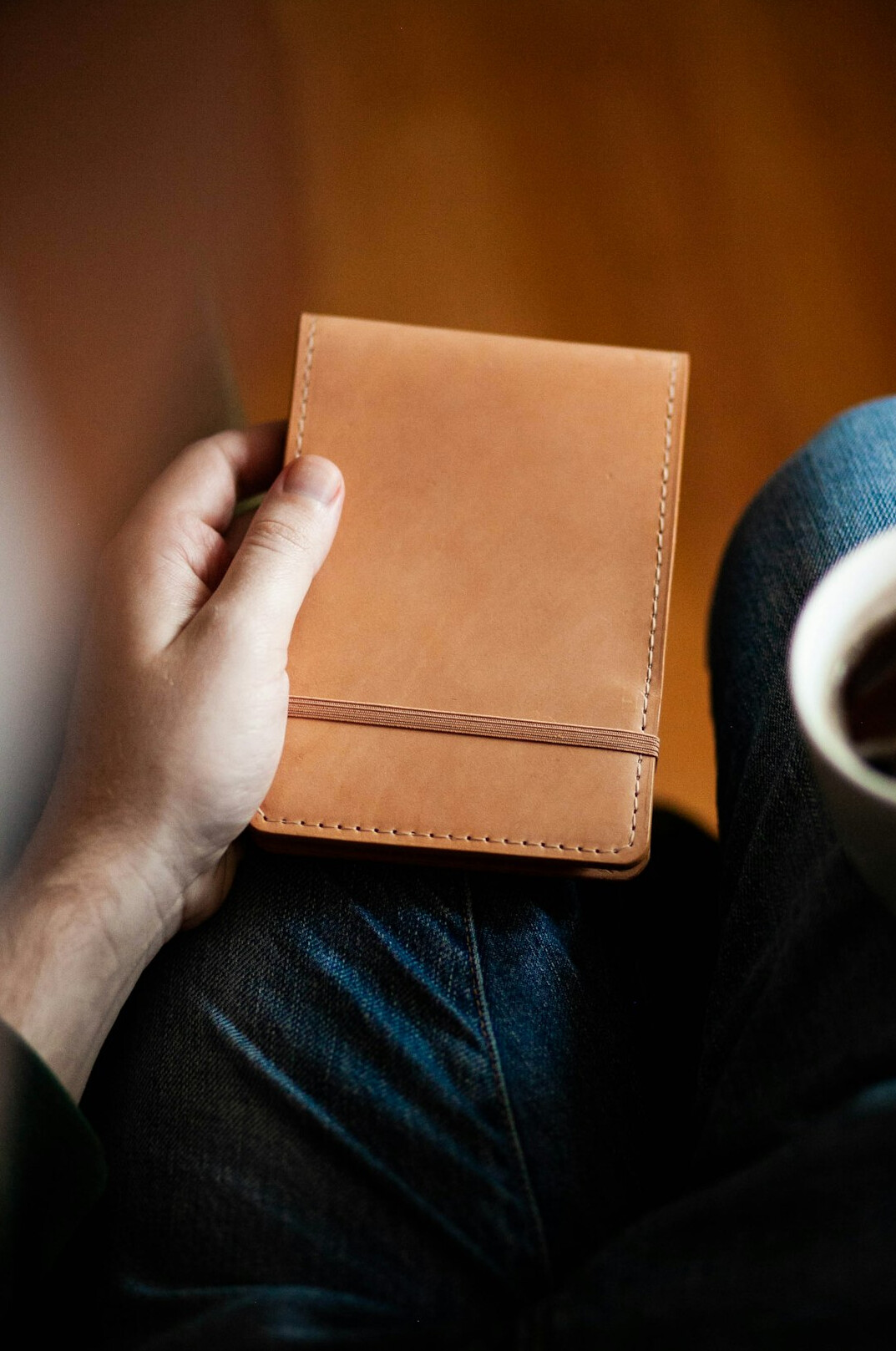 Hands writing in a leather notebook next to a cup of coffee